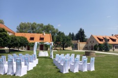 Historické nádvoří zámku Libouchec připravené pro letní svatbu s bílými židlemi a květinovou bránou.