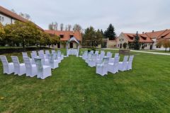 Historické nádvoří zámku Libouchec připravené pro letní svatbu s bílými židlemi a květinovou bránou.