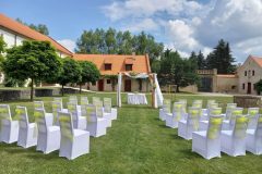 Historické nádvoří zámku Libouchec připravené pro letní svatbu s bílými židlemi a květinovou bránou.